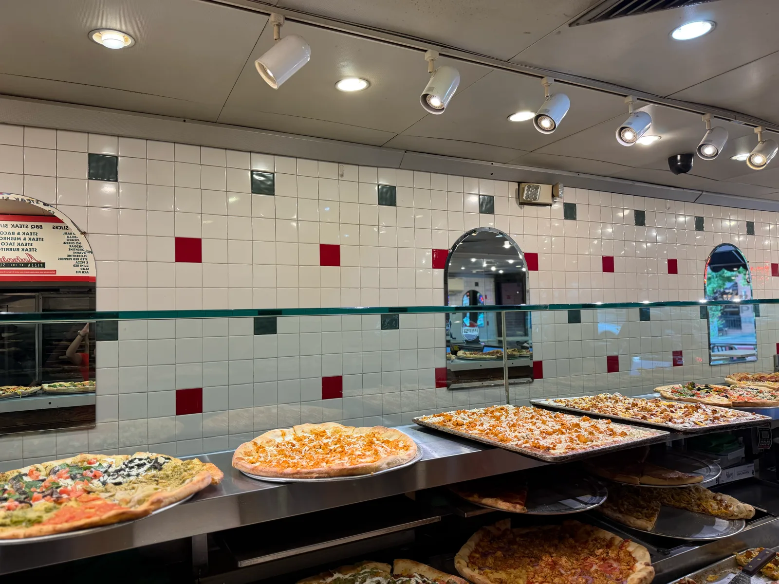 Tiled slice display wall lined with whole pizzas and fresh slices at Antonio's Pizza Amherst