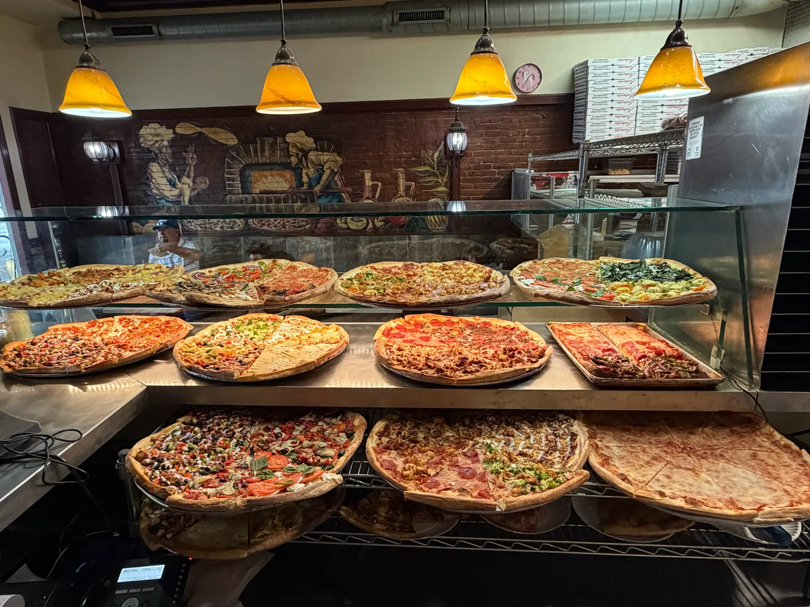 Antonio's Easthampton slice display lined with whole pizzas under warm pendant lights