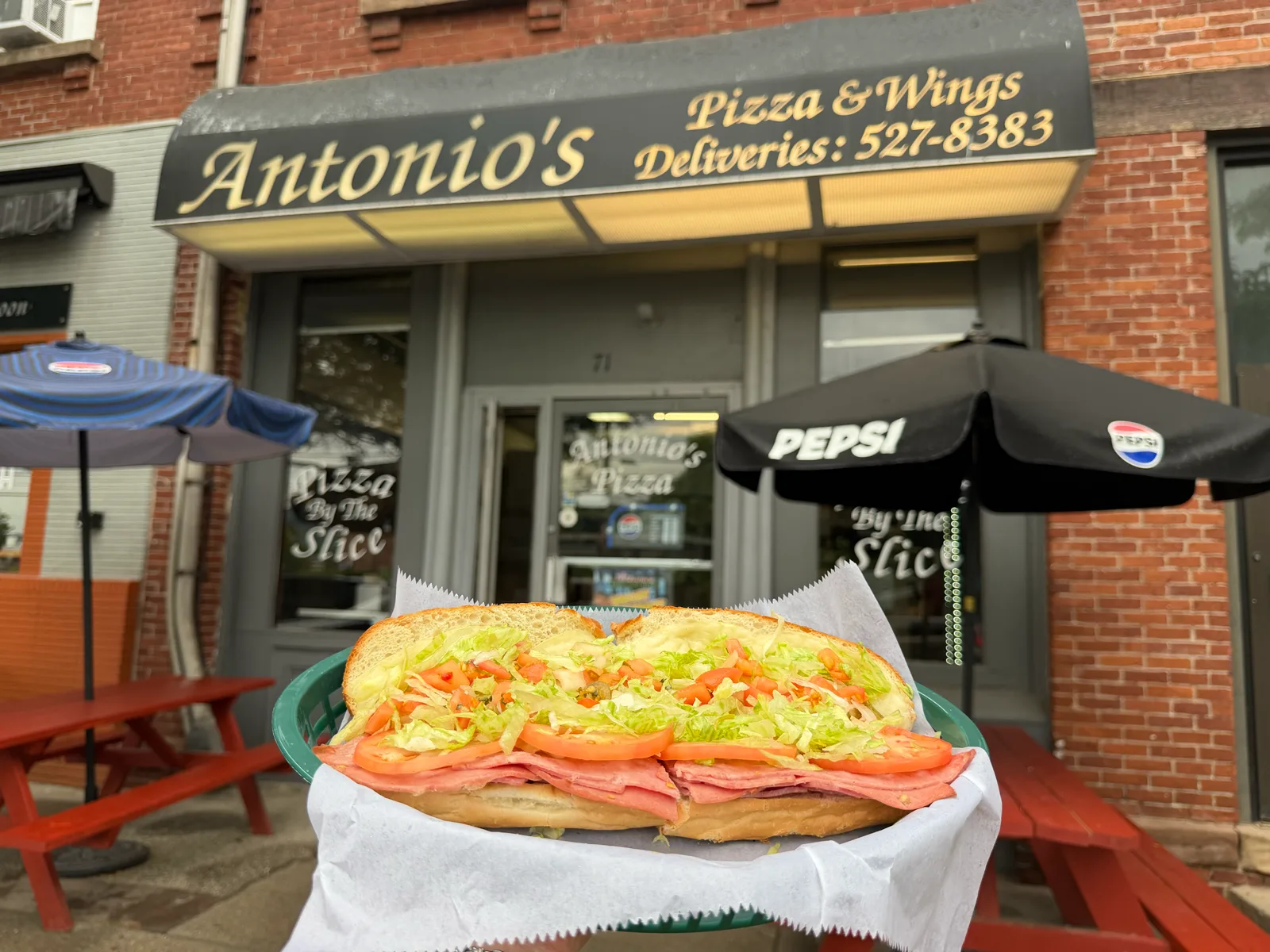 A 12-inch Italian sub held in front of the Antonio's Easthampton storefront