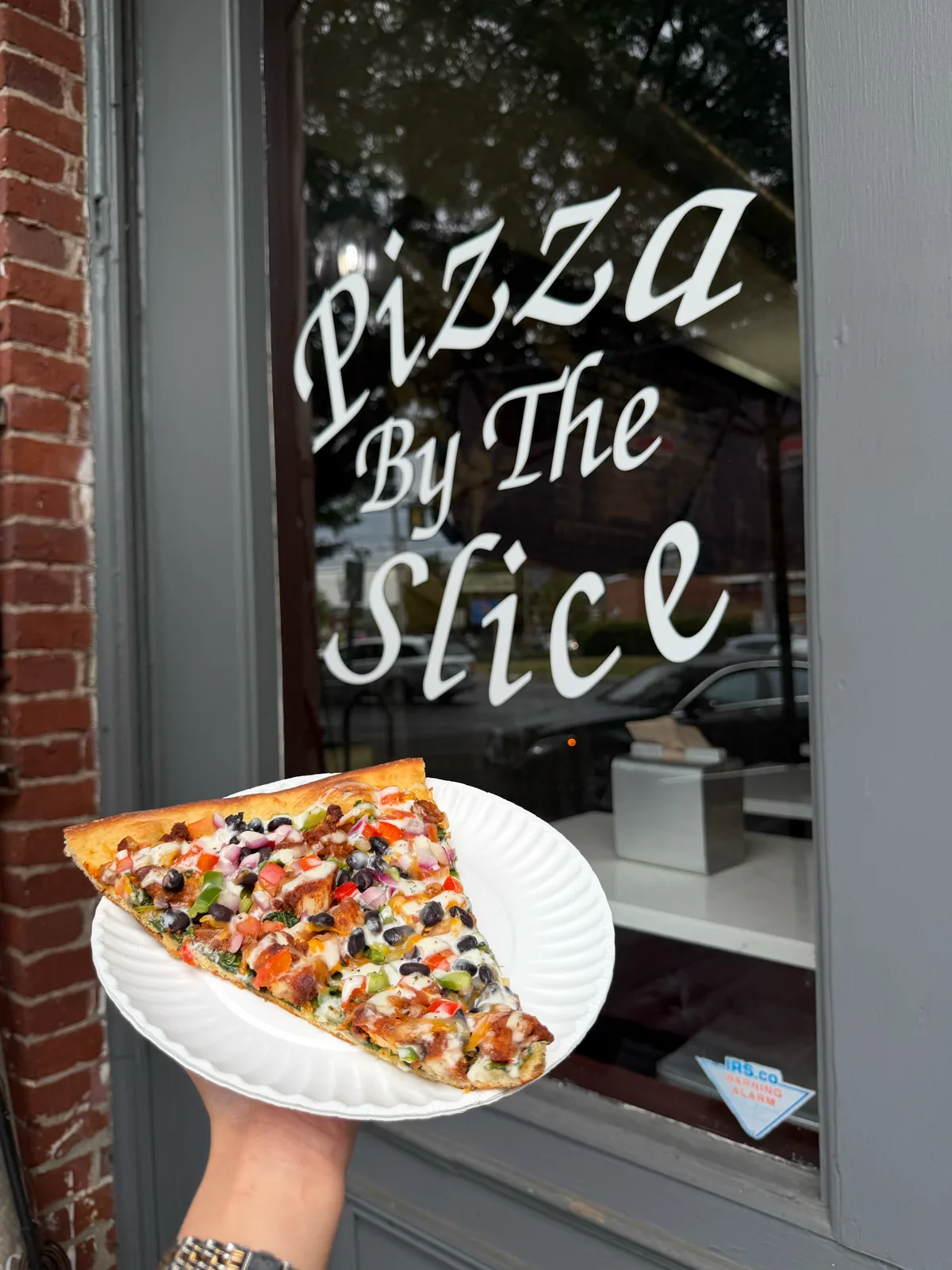 A loaded gourmet slice held at Antonio's "Pizza By The Slice" window