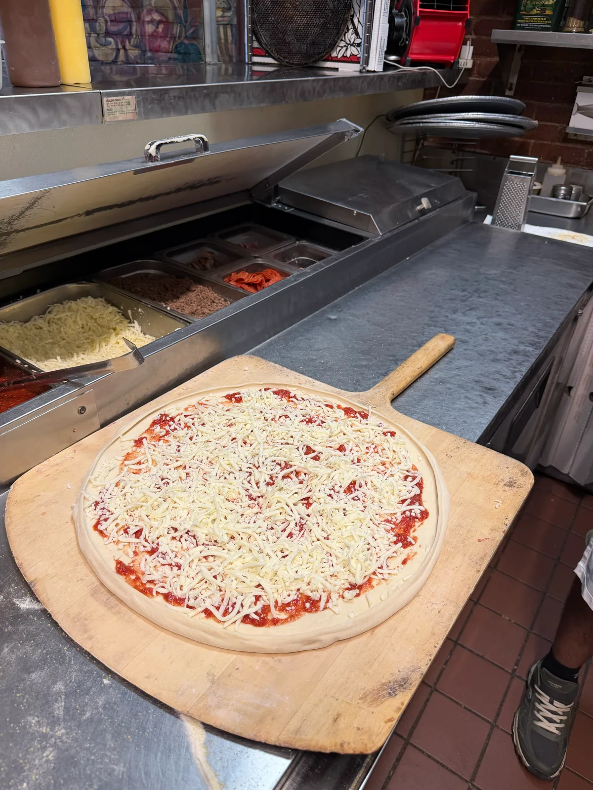 A fresh cheese pizza on the peel by the topping station at Antonio's Easthampton