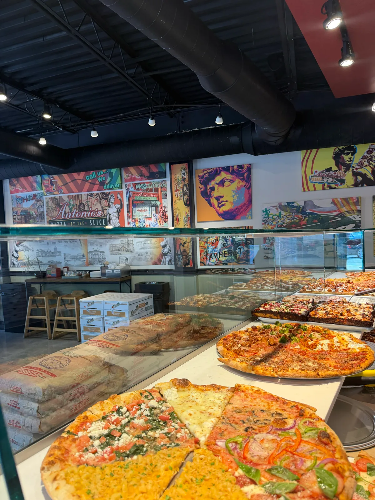 Antonio's Bellevue slice display case with whole pizzas and pop-art murals along the wall