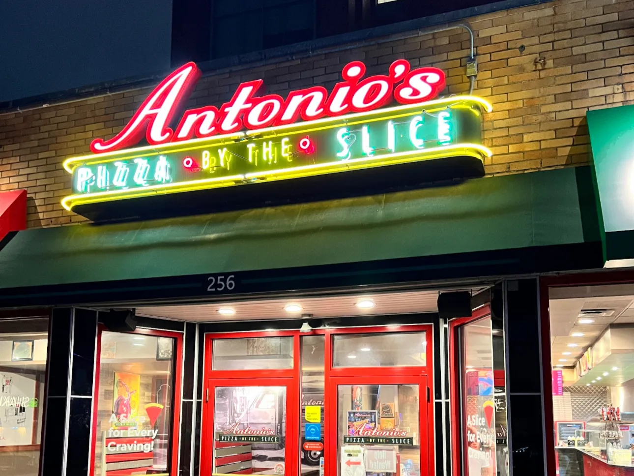The Antonio's Pizza by the Slice neon sign glowing over the 256 Thayer Street entrance at night