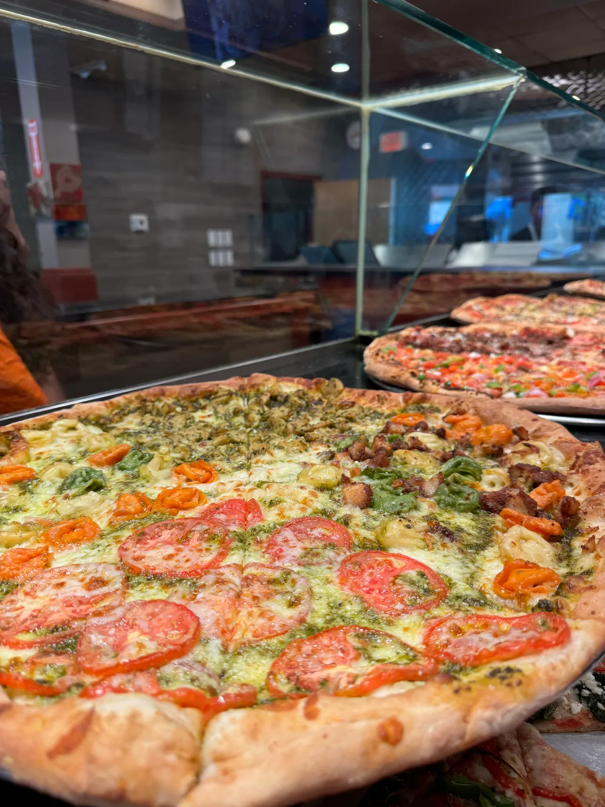 Antonio's pesto pie topped with fresh tomato slices in the slice display