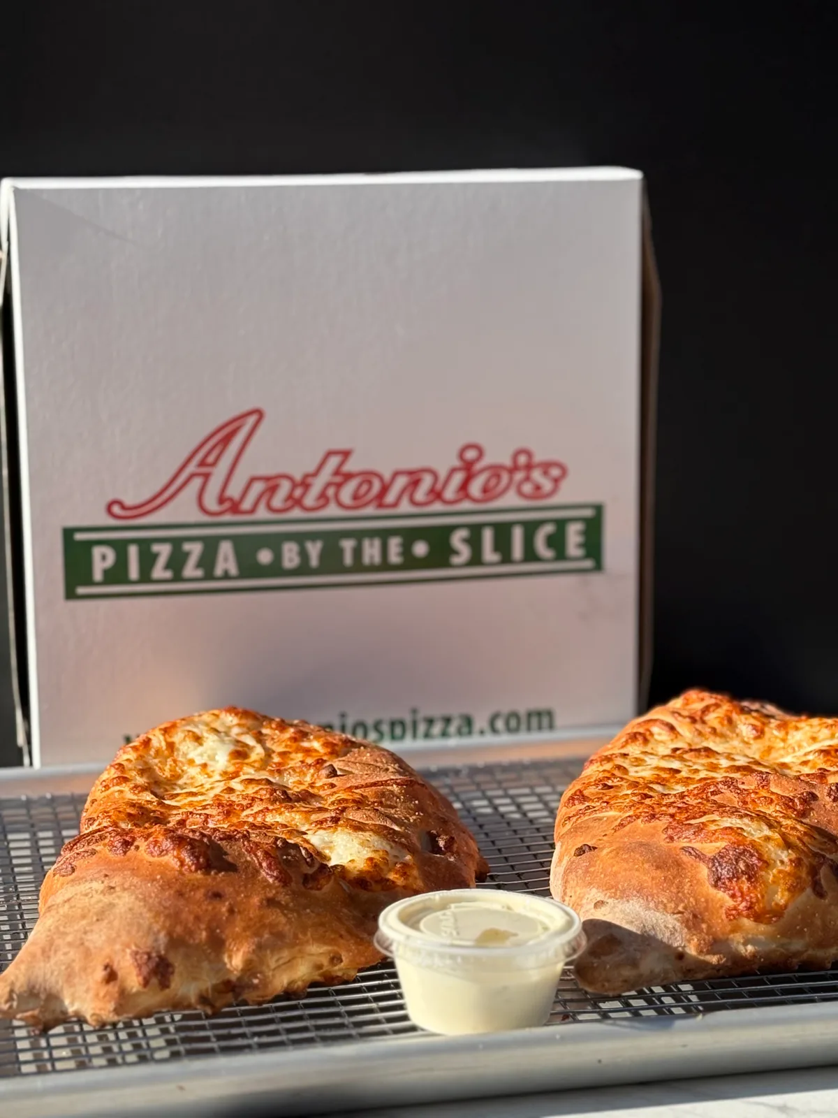 Two golden calzones with dipping sauce in front of an Antonio's pizza box