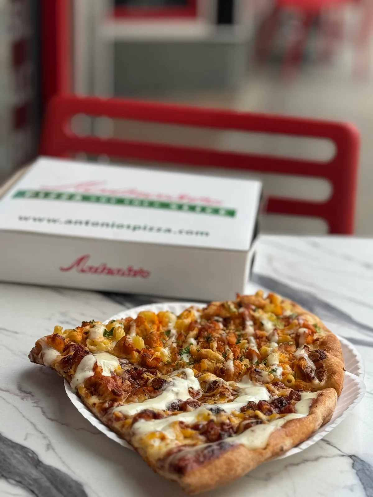 Antonio's slices on a paper plate in front of a branded pizza box